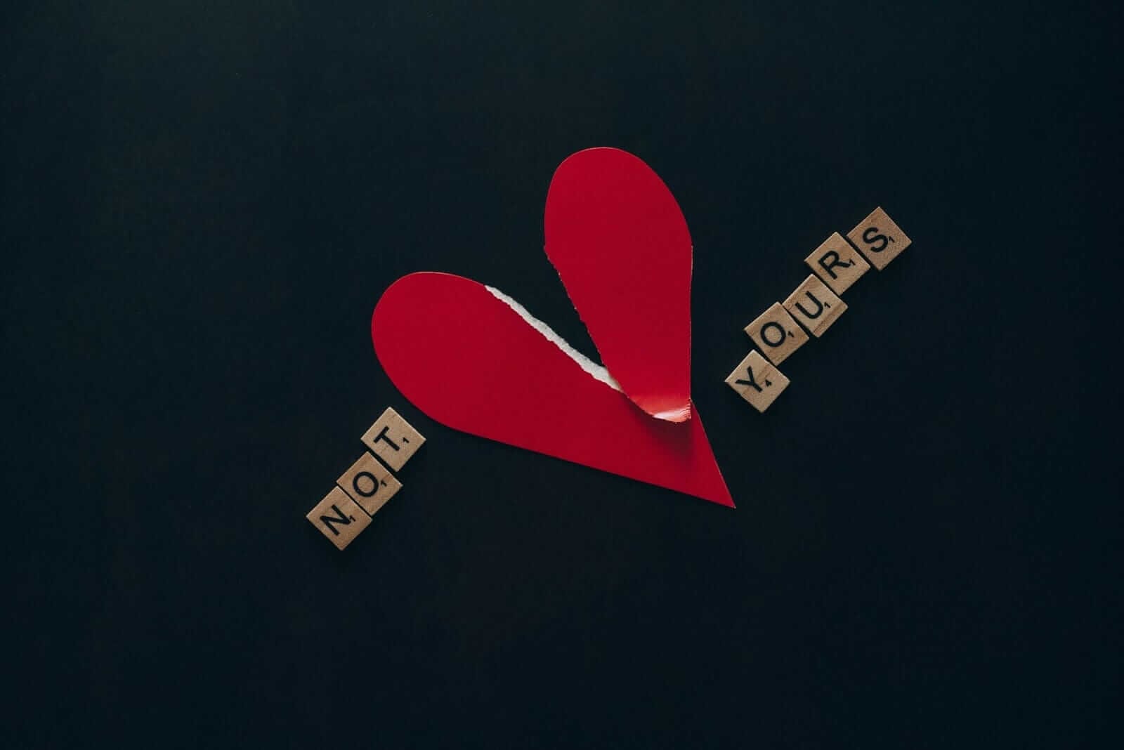 a torn paper heart with NOT YOURS spelled out in scrabble tiles